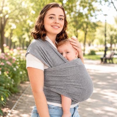 Jeune maman utilisant une écharpe de portage Mon Petit Cocon™ lors d’une promenade extérieure avec bébé installé confortablement